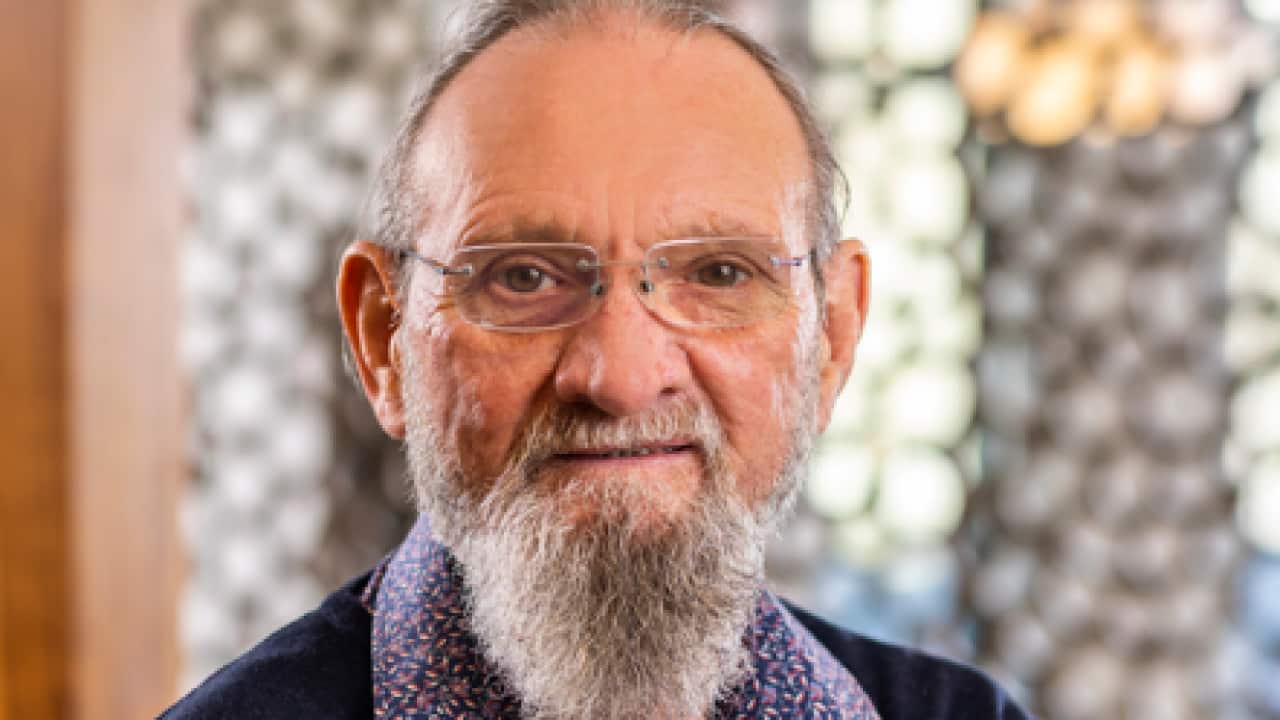 an older man with a long grey beard wearing glasses smiling at the camera
