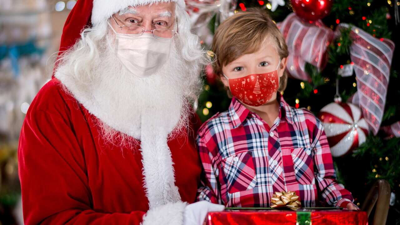 Portrait of a little boy with Santa wearing facemasks while getting a gift