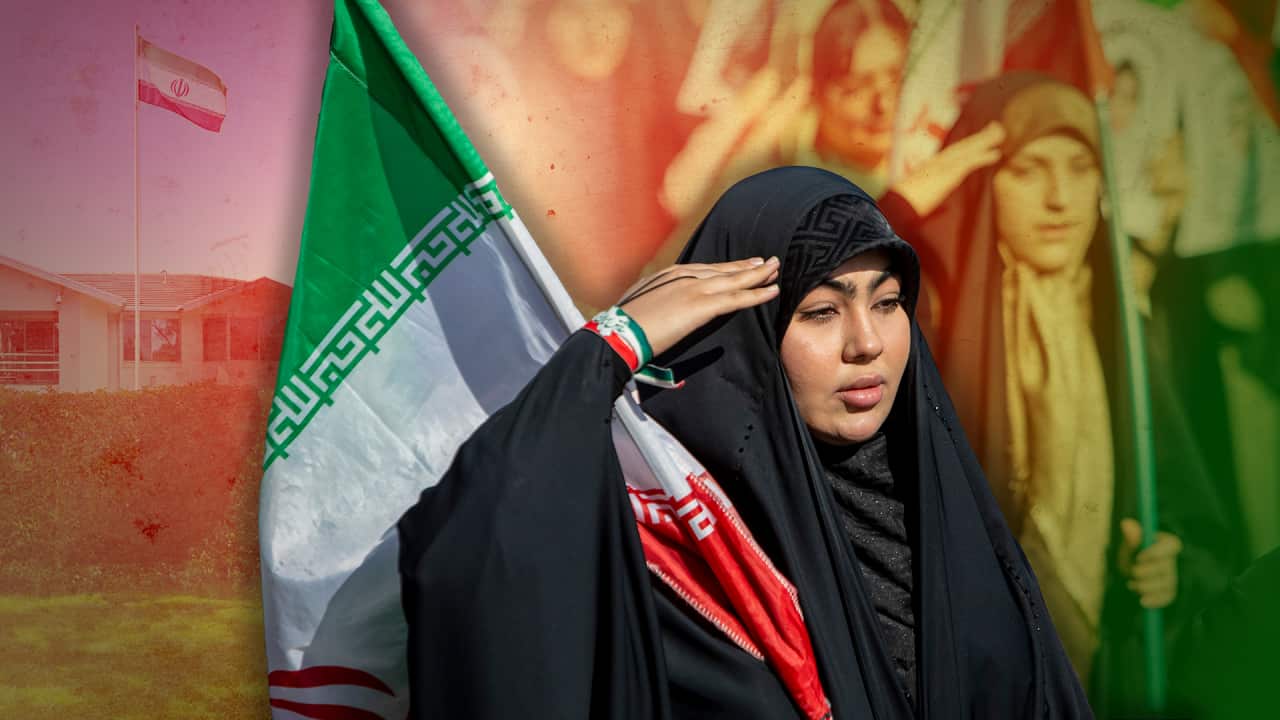 Iranian woman in black hijab saluting with Iranian flag, composite image of embassy and crowd in background.