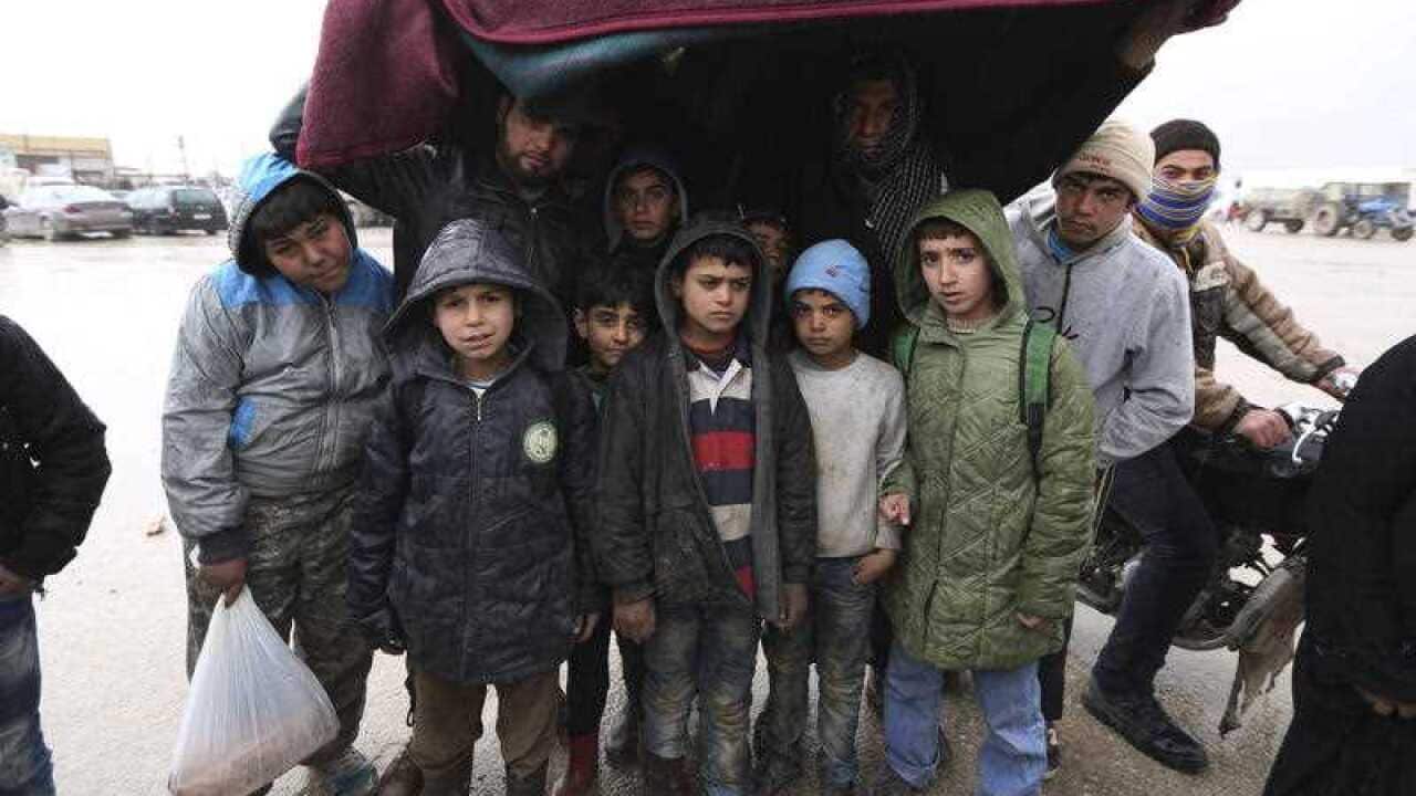 Syrians try to protect themselves from rain near the Bab al-Salam border crossing with Turkey