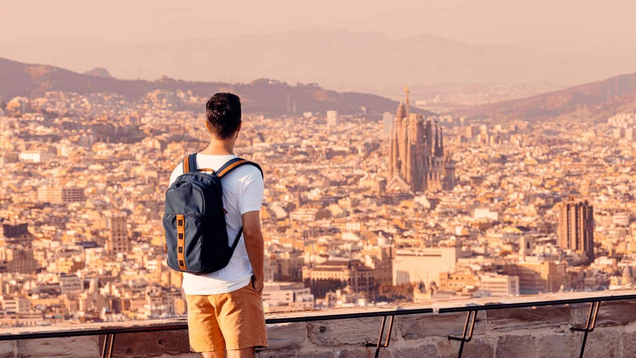 Tourist with backpack looking at Sagrada Familia and Barcelona skyline from above, Spain