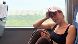a young woman in a cap sitting on a train with her elbow resting against the window