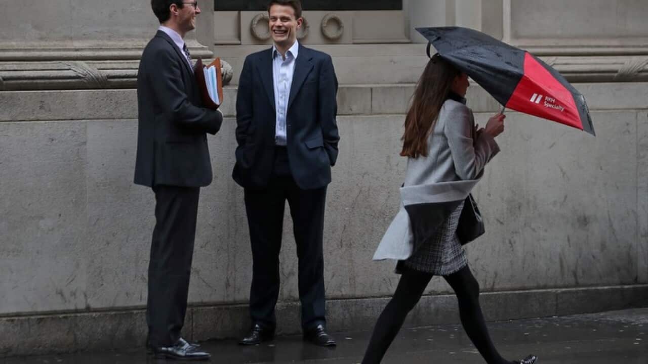 A woman walks past two men on the street. All three are wearing business attire.