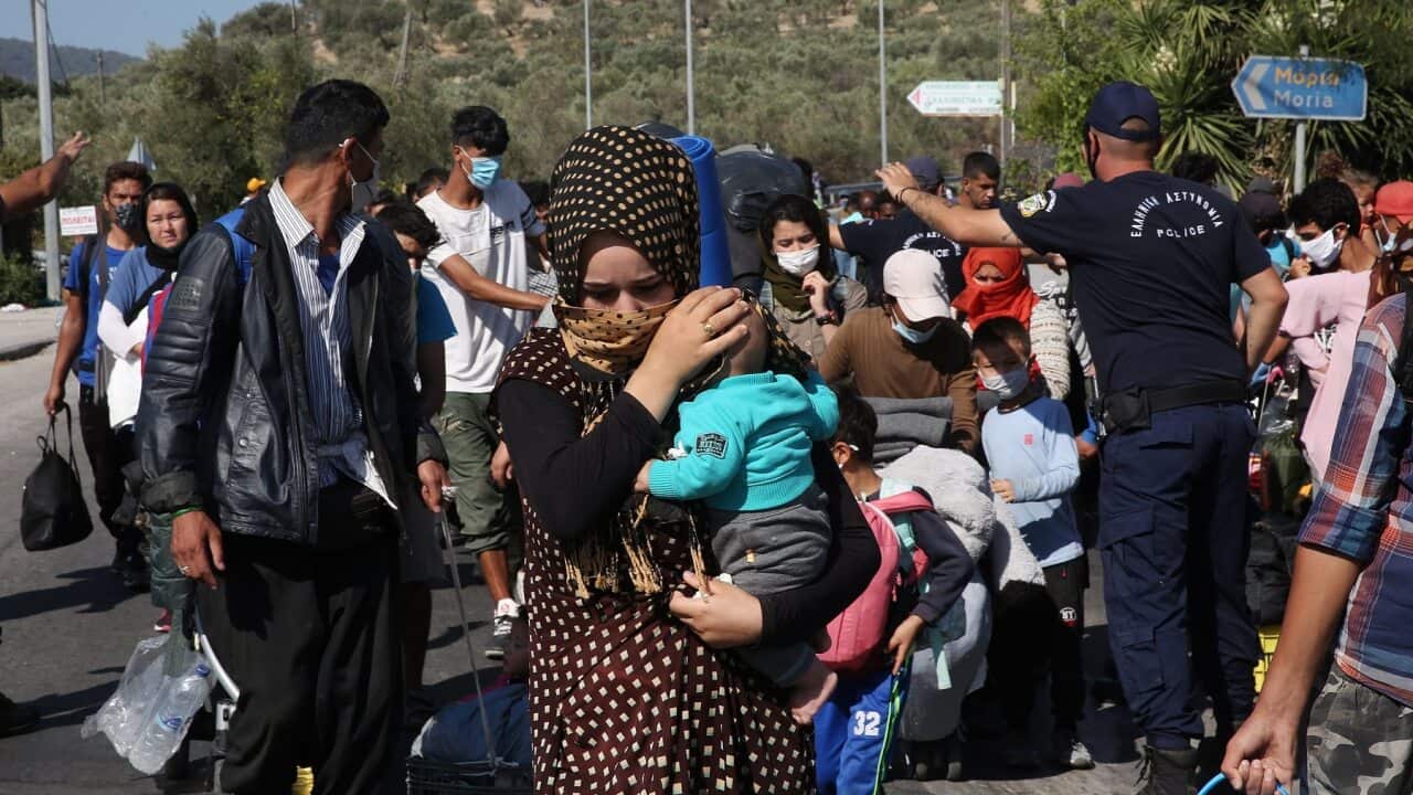 Asylum seekers carry their belongings as they walk on a roadside, near the destroyed Moria refugees camp.