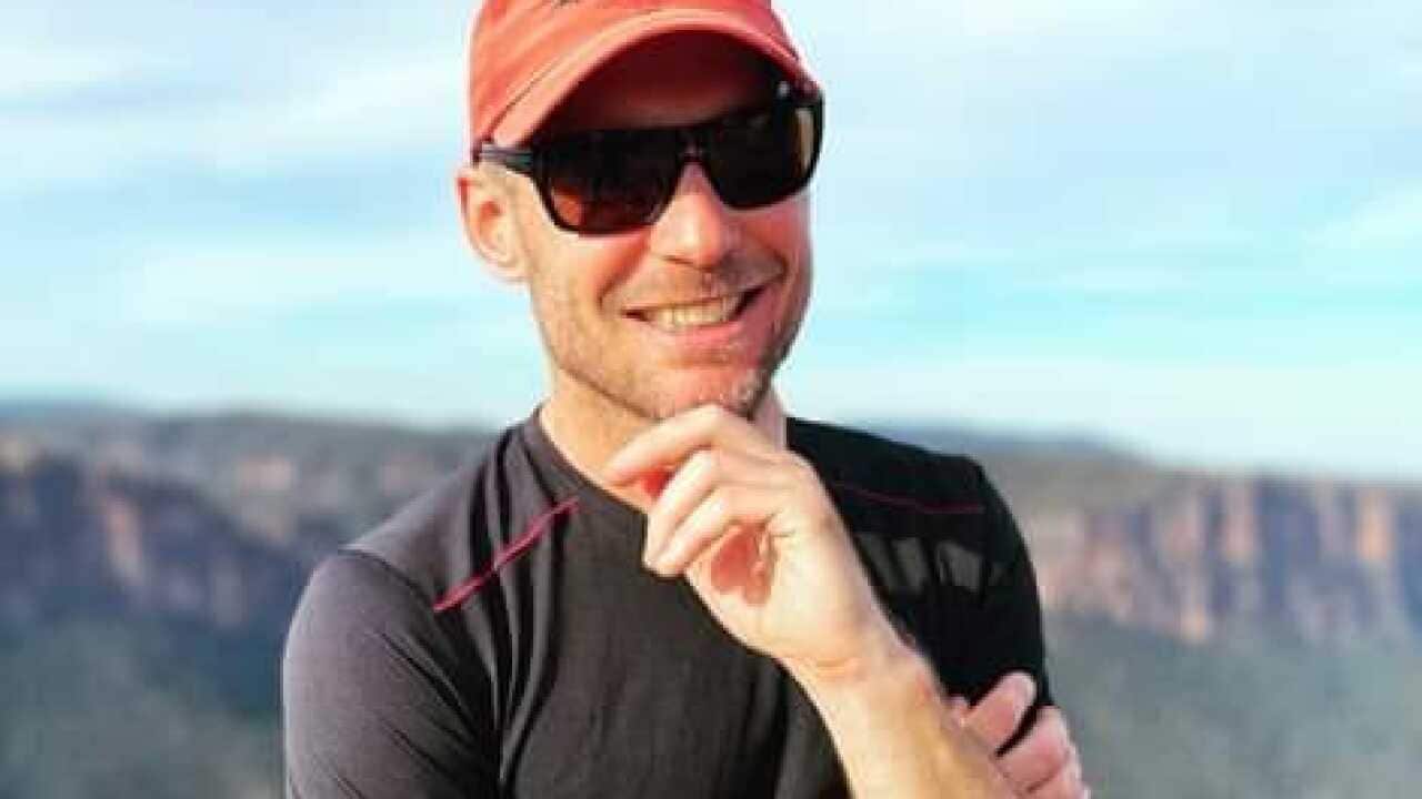A man smiles with a view of mountains behind him