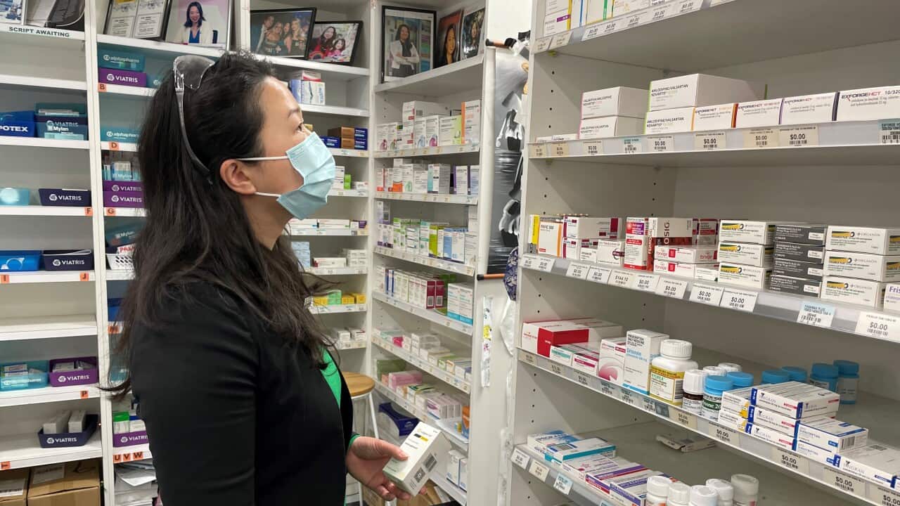 Woman wearing a face mask standing in front of a row of medicines.