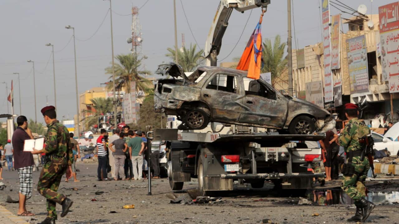 Security forces watch a tow truck lift a destroyed vehicle