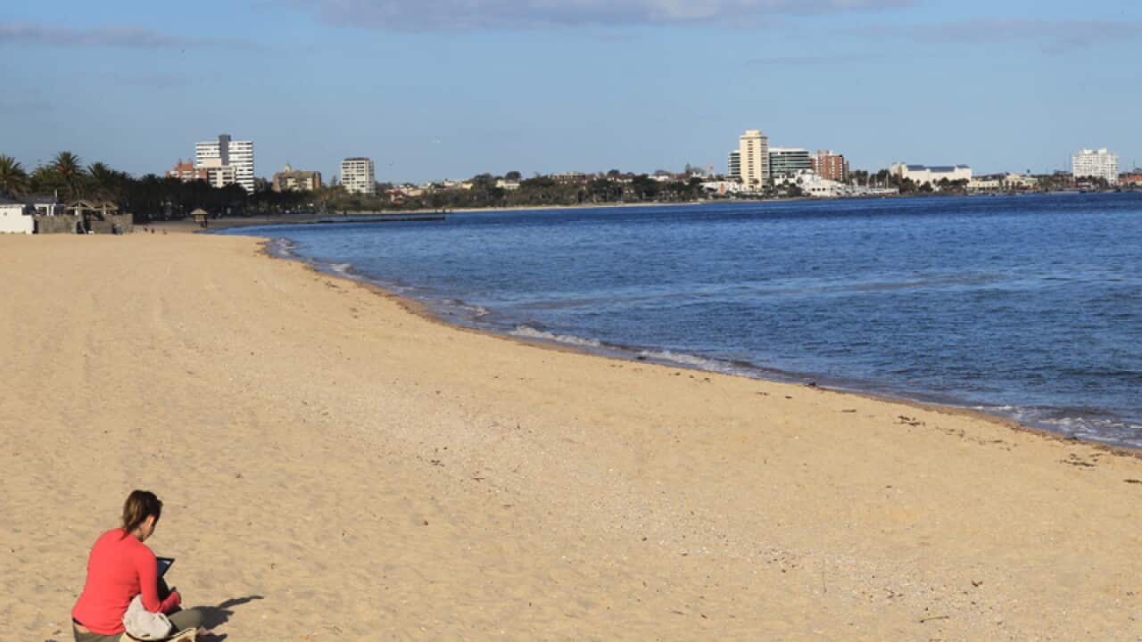 A woman sits on a beach on the Port Phillip Bay foreshore in Melbourne