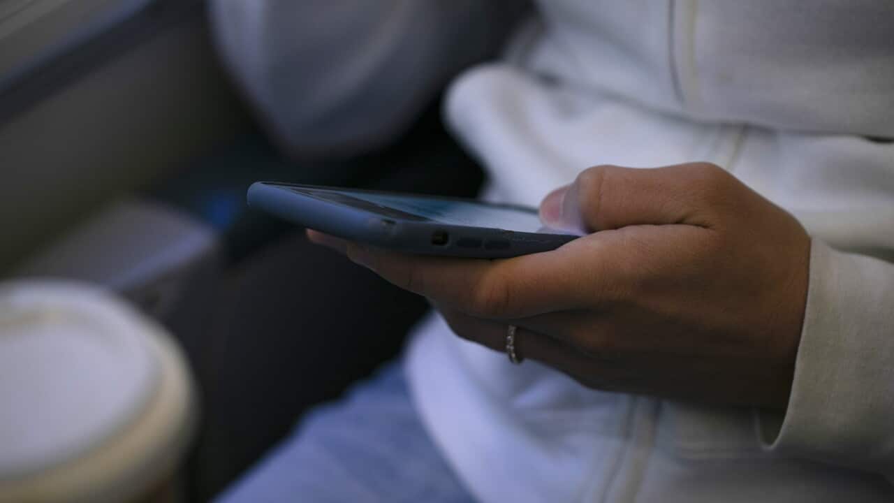 A woman wearing a white jumper and holds a phone in her palm. She wears a small silver ring on her finger.