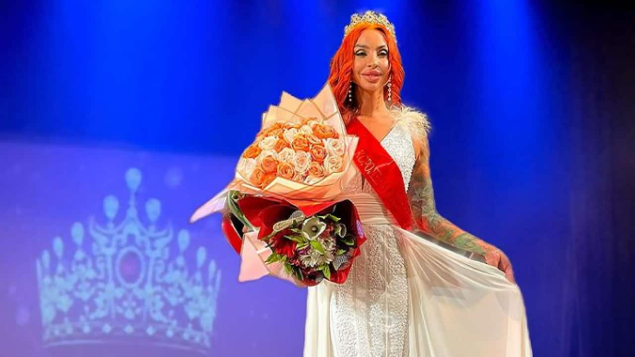 A woman stands in a dress with flowers and crown.