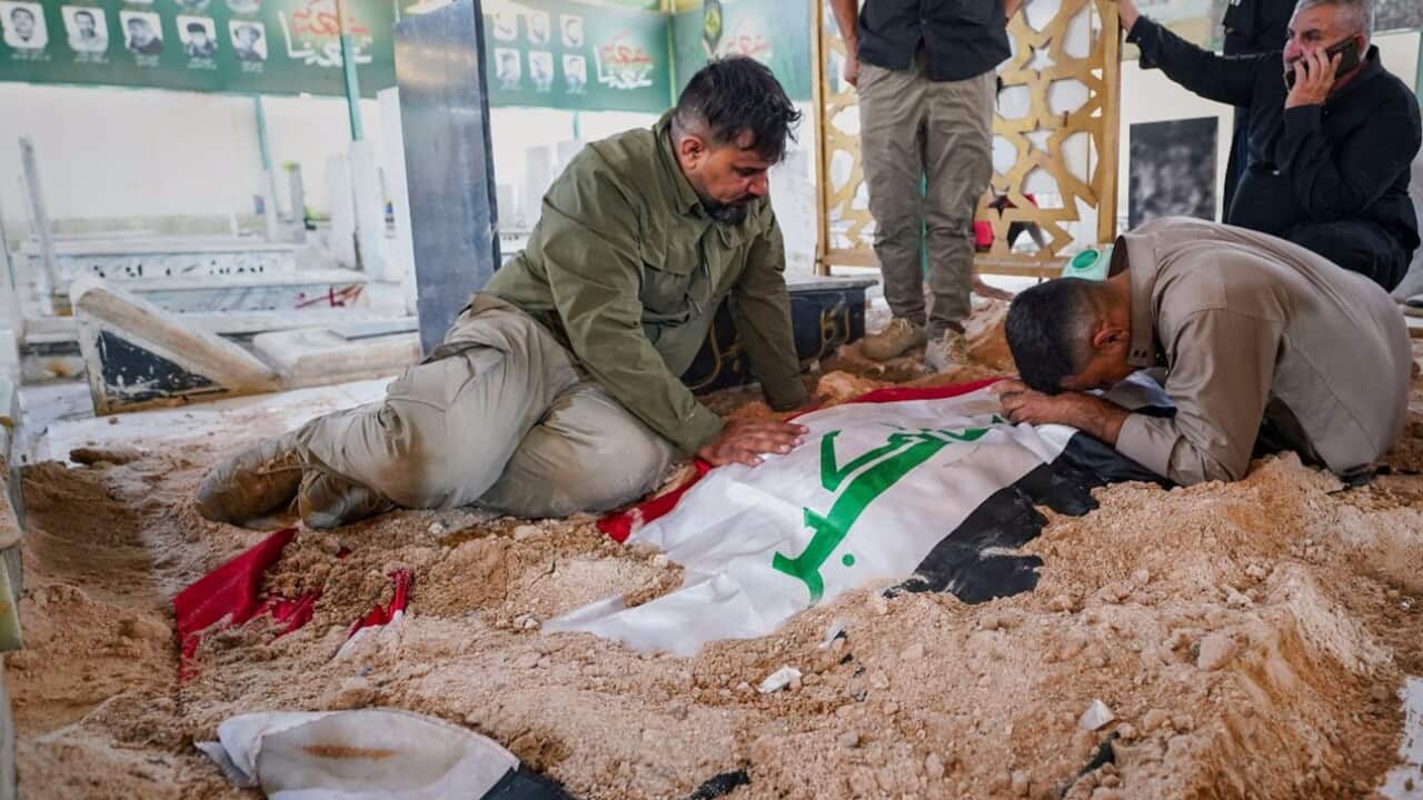 Mourners grieve beside a grave of fighters killed in airstrikes on PMF bases in Najaf, Iraq.jpg