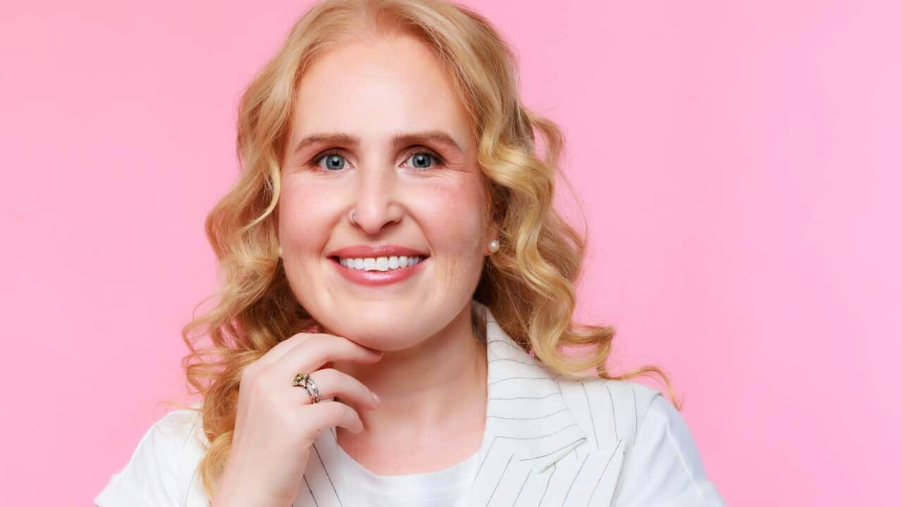 A woman with long blonde hair in a white T shirt and waistcoat smiles at the camera.