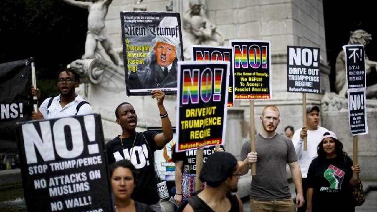 A small group of people gather with signs to protest today's decision by the United States Supreme Court to reinstate a portion of President Donald Trump's executive order prohibiting people from certain countries