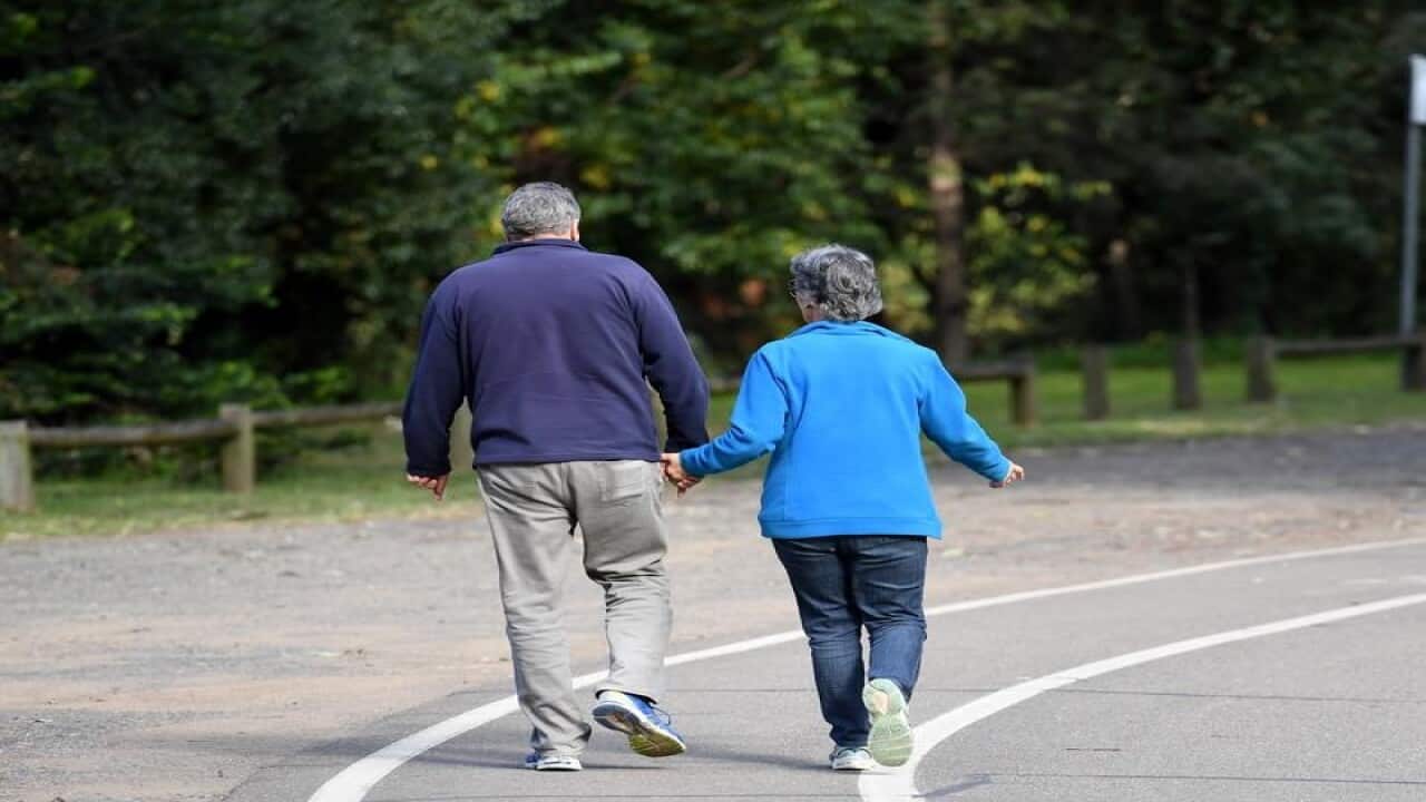 An elderly couple walk through a park