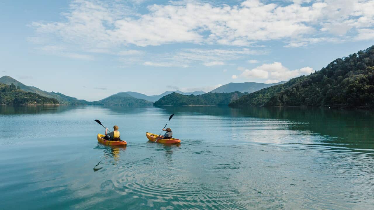 Two people canoeing side by side on remote lake with hill surrounds