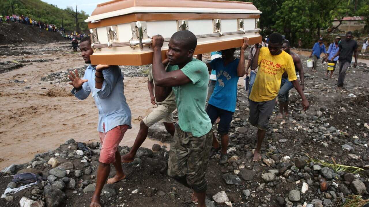A group of people carry a coffin and try to cross the river La Digue, after the colapse of a bridge in Haiti
