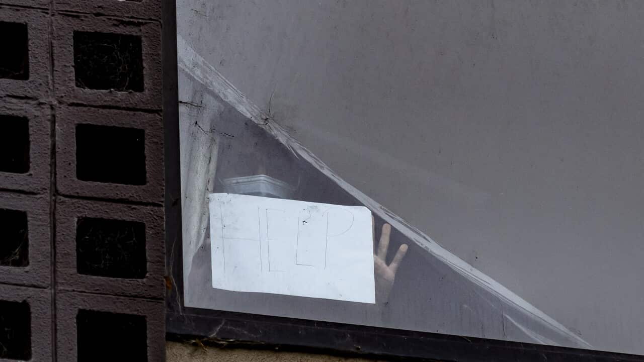 A person holds up a sign reading ‘help’ from a window of the Park Hotel in Carlton as refugee advocates rally across the road in Melbourne