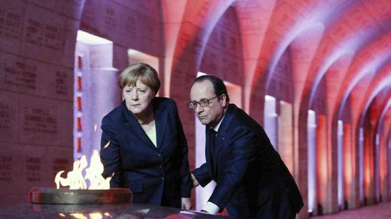 French President Francois Hollande, right, and German Chancellor Angela Merkel revive the Eternal Flame at the Douaumont's Ossuary, in Douaumont