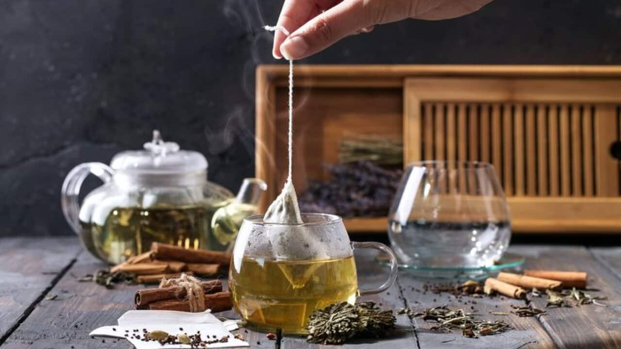 Tea bag being brewed in cup, spices and leaves around it