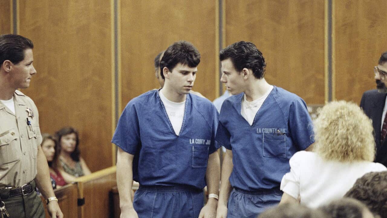 Two men in blue jumpsuits speaking to each other in a courtroom.