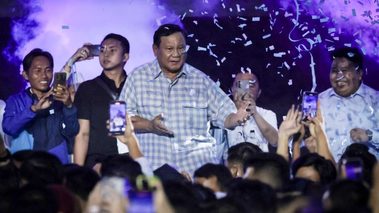 A man in a chequered shirt dances on a stage as confetti rains down from above.