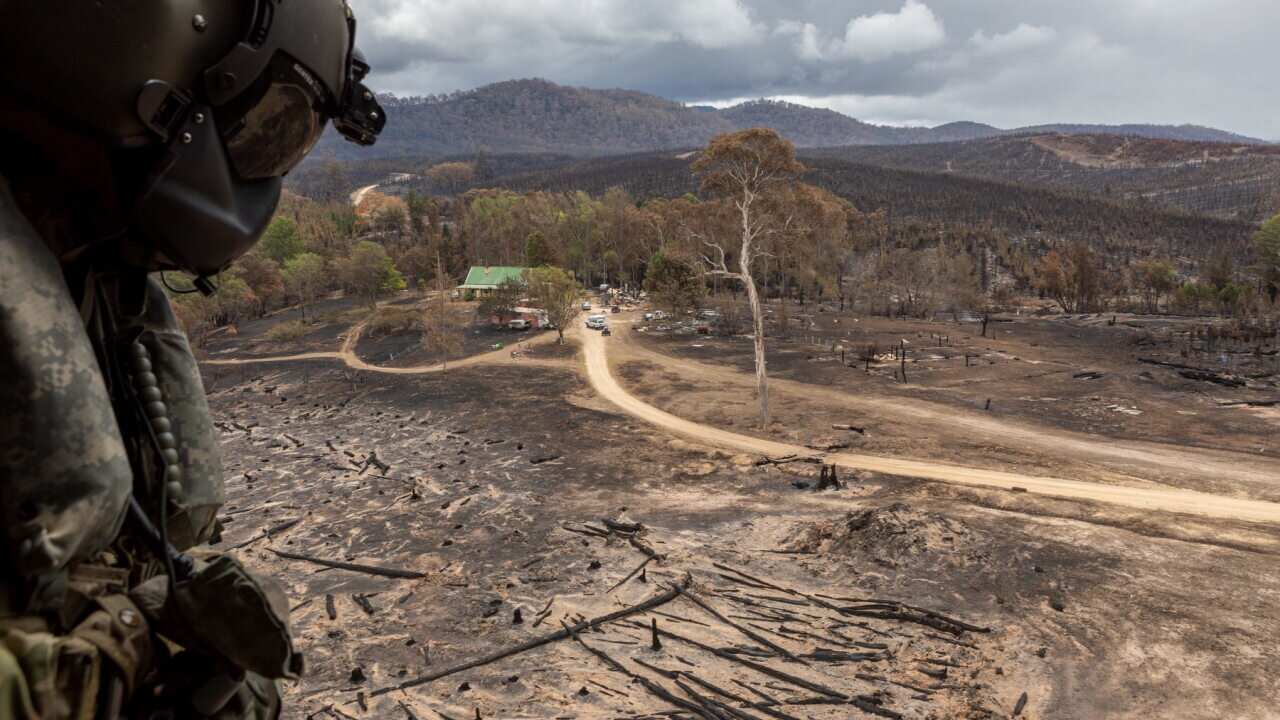 The Royal Australian Navy's Brendan Menz keeps watch as a helicopter lands in a burnt out field in southern New South Wales, Australia, 9 January 2020.