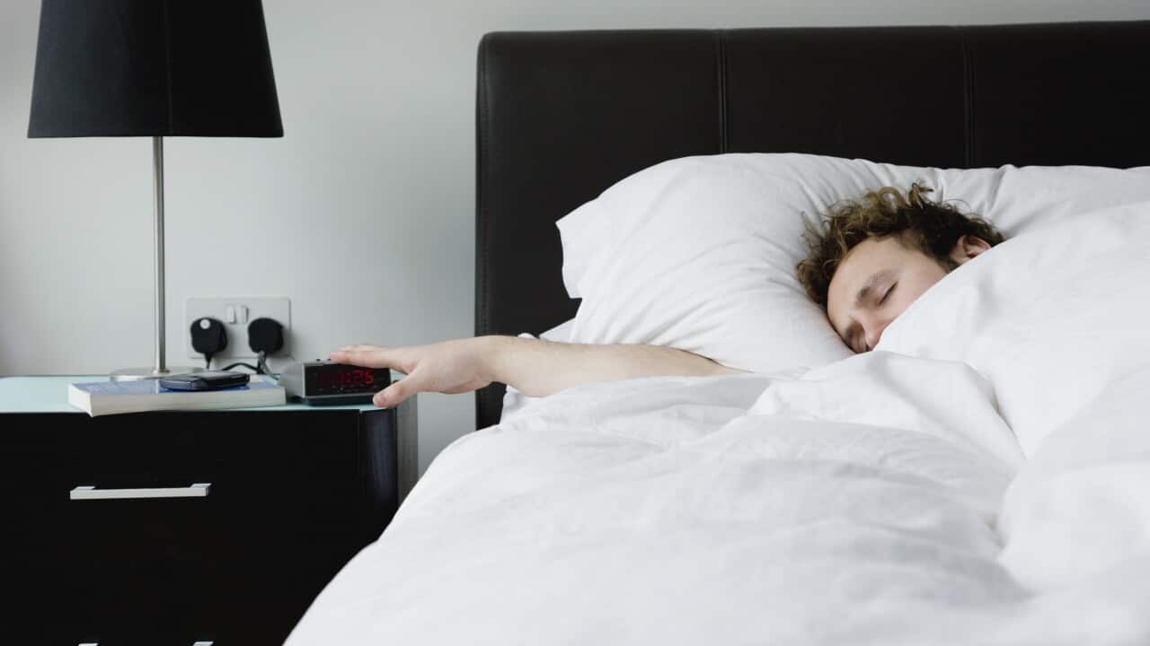Man holding hand on alarm clock lying in bed