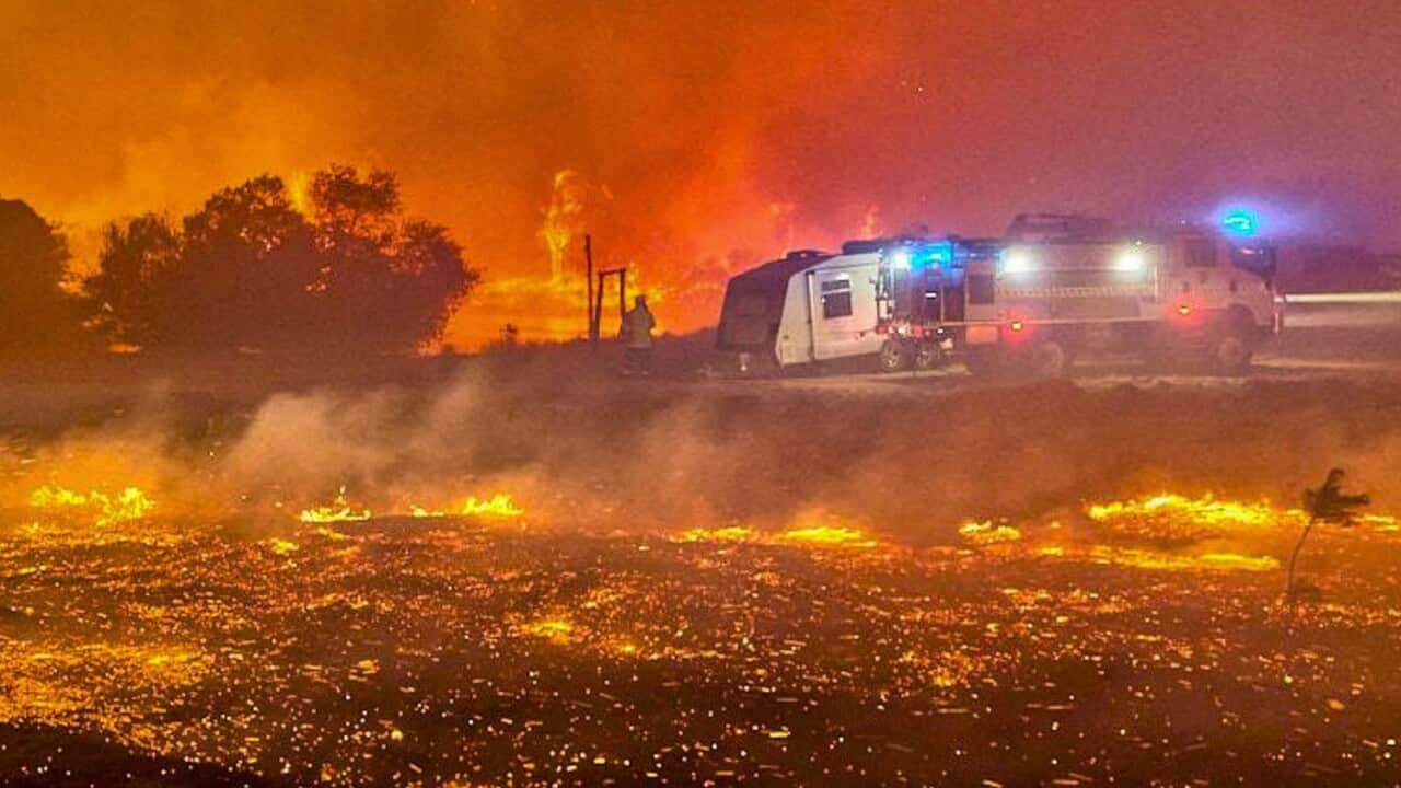 A bushfire raging with emergency services vehicles in the background.