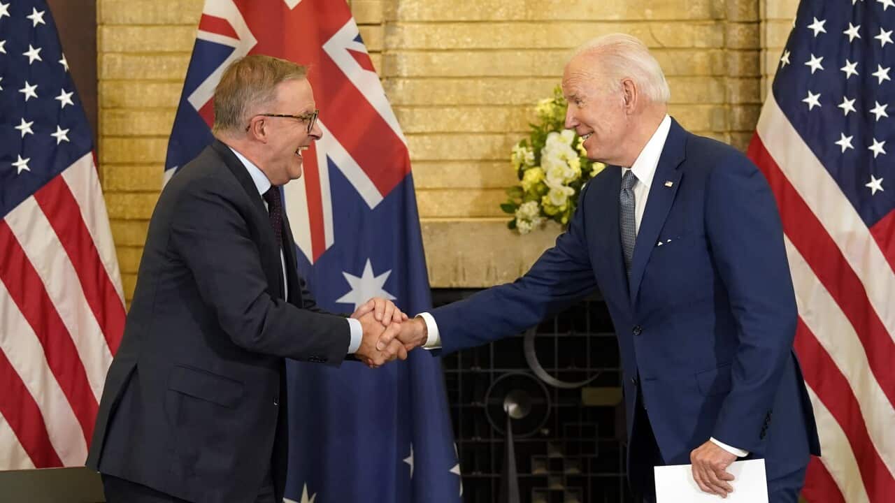 Two men in suits shaking hands with American and Australian flags in backround