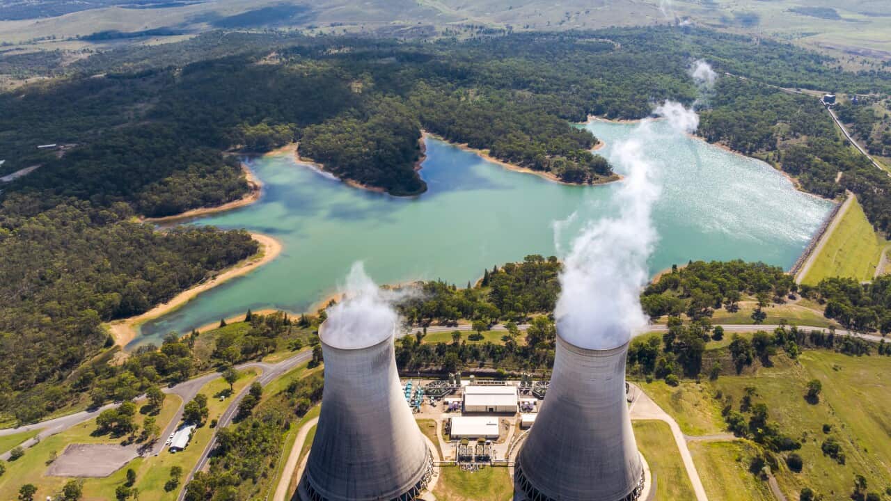 Aerial shot of 2 energy power stations emitting gas smoke next to a lake and green fields
