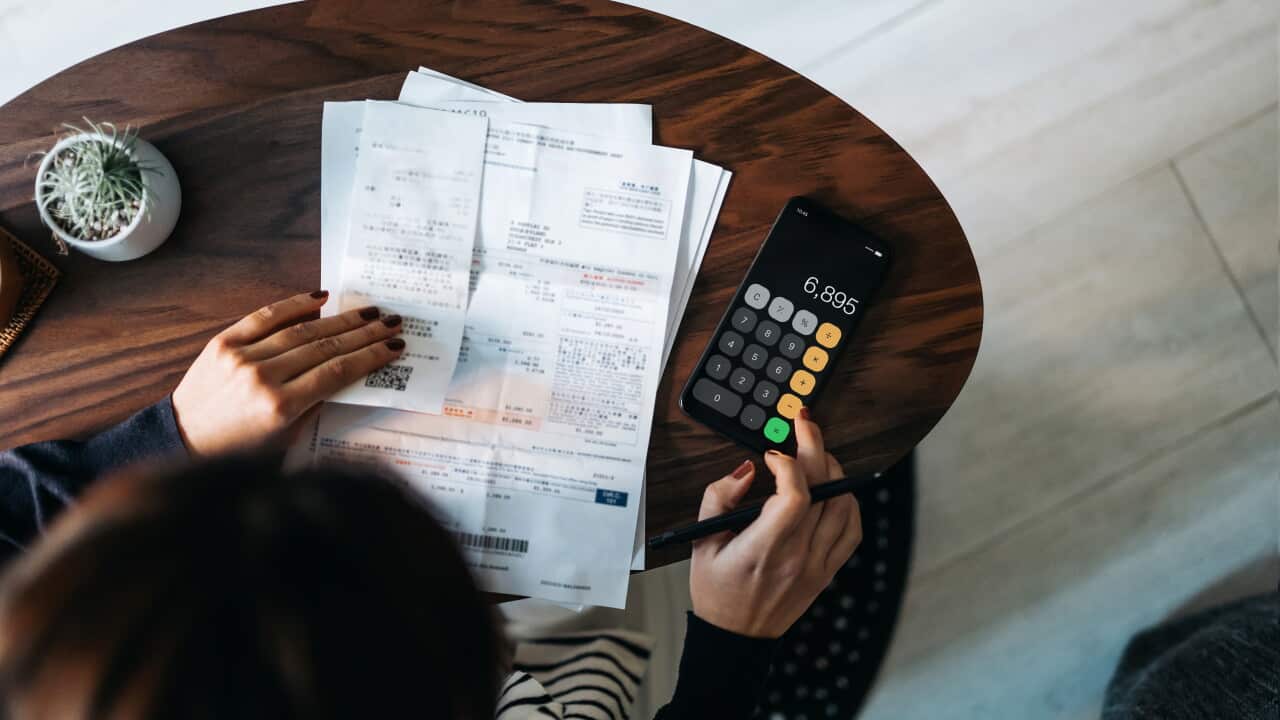 Overhead view of young woman with paper bills and a calculator in front of her.