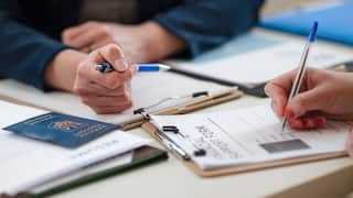 Close-up of two people filling in a paper form and Ukrainian passport.