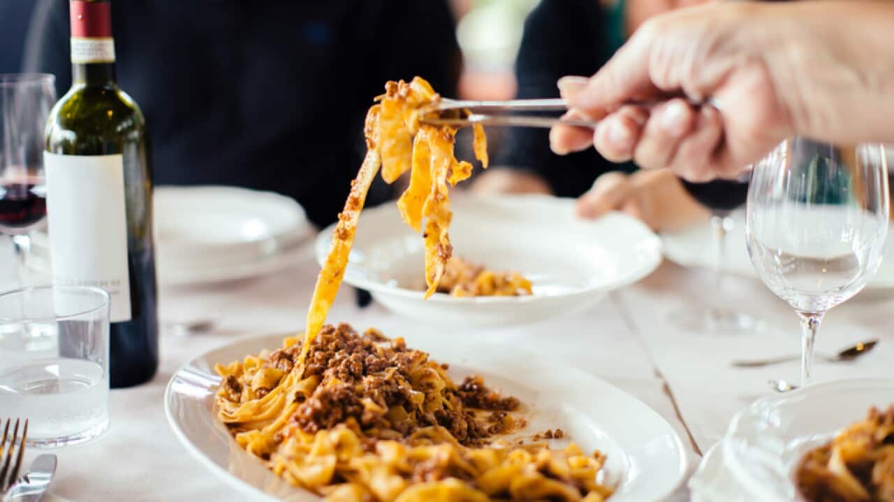 Womans hand serving tagliatelle with ragu sauce at table