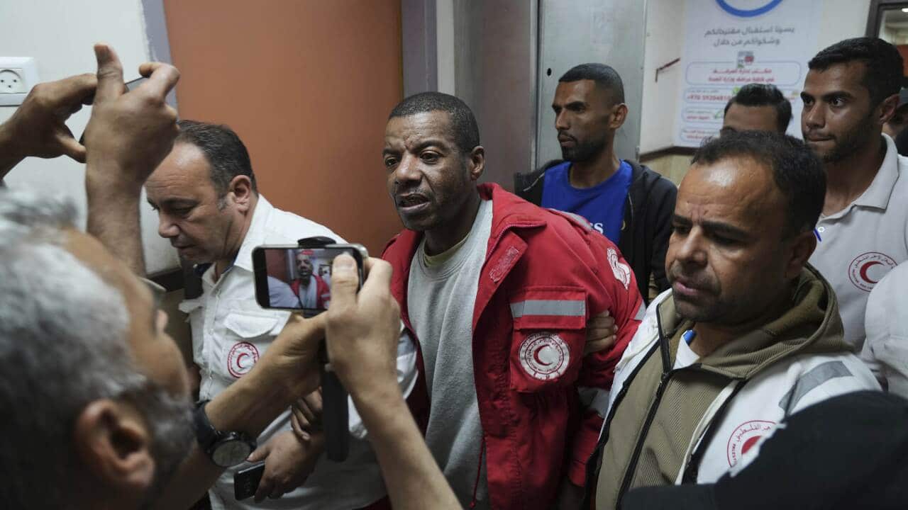 A man in a red jacket is being escorted by Red Crescent workers as two men take his pictures on their phones.
