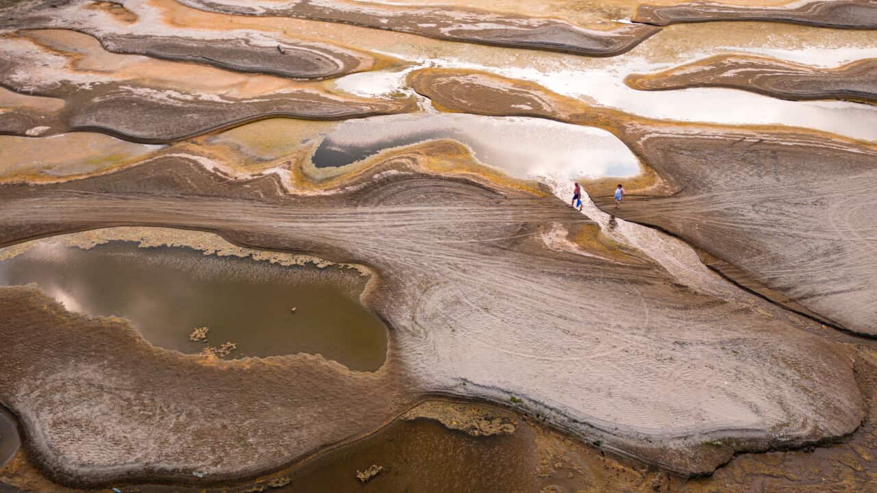 People walk along dry yellow and brown sandbanks along the Danube River in Romania.