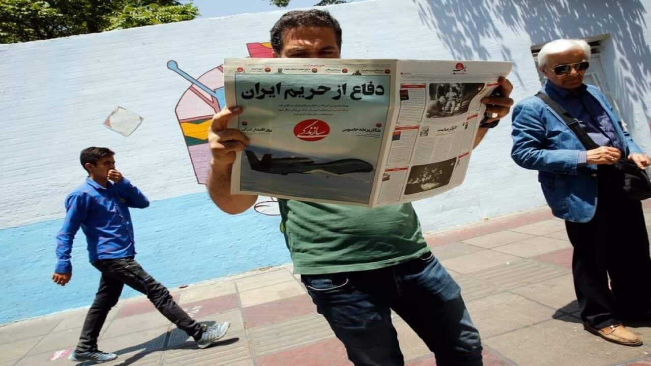 An Iranian man reads a newspaper about the shooting down of the drone