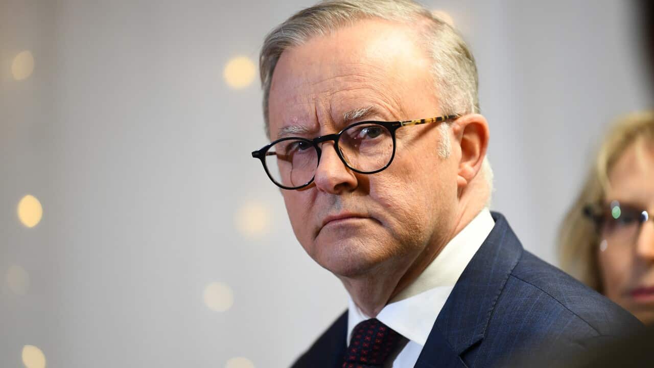 A man wearing a suit, tie and glasses listens as someone speaks.