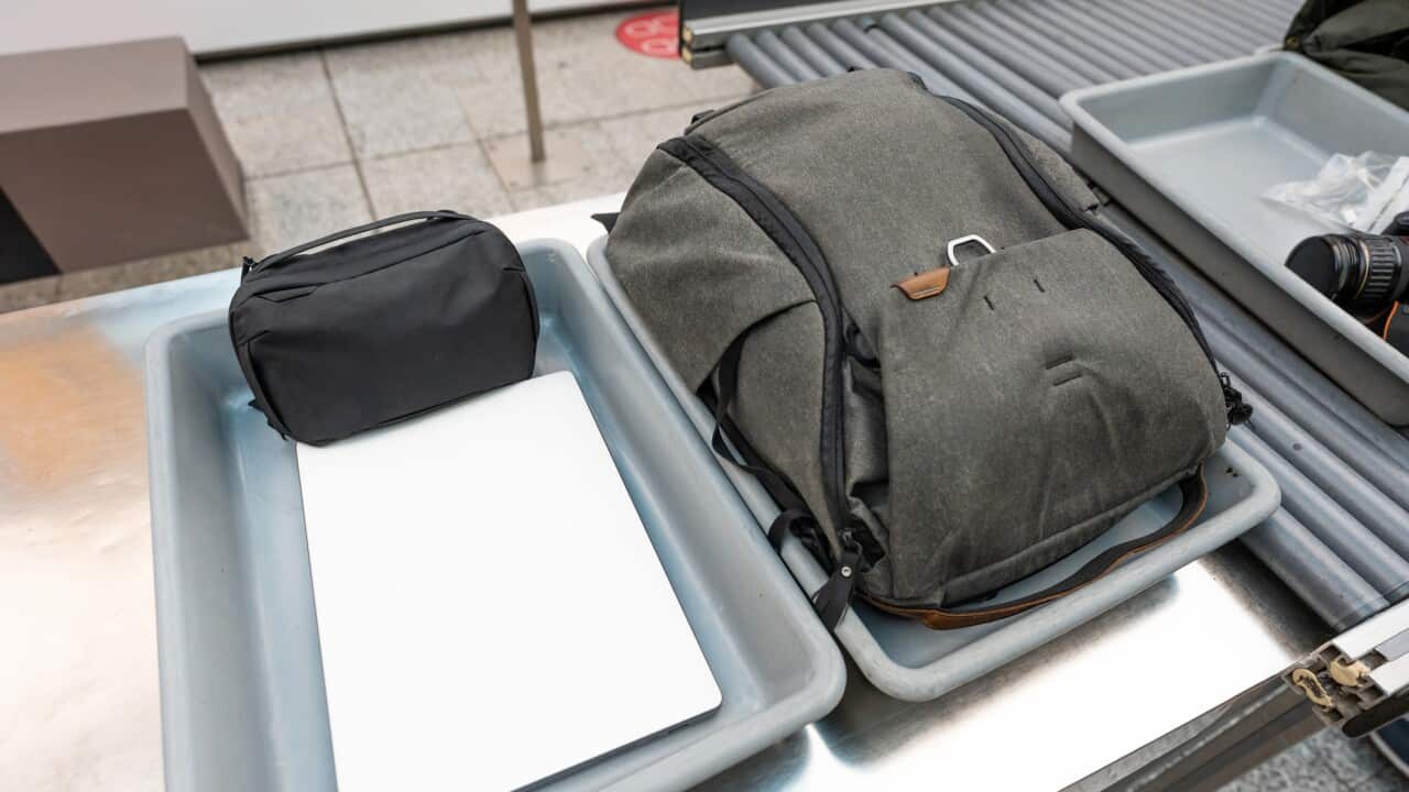 Airplane carry-on luggages placed on security control trays with electronic equipment outside