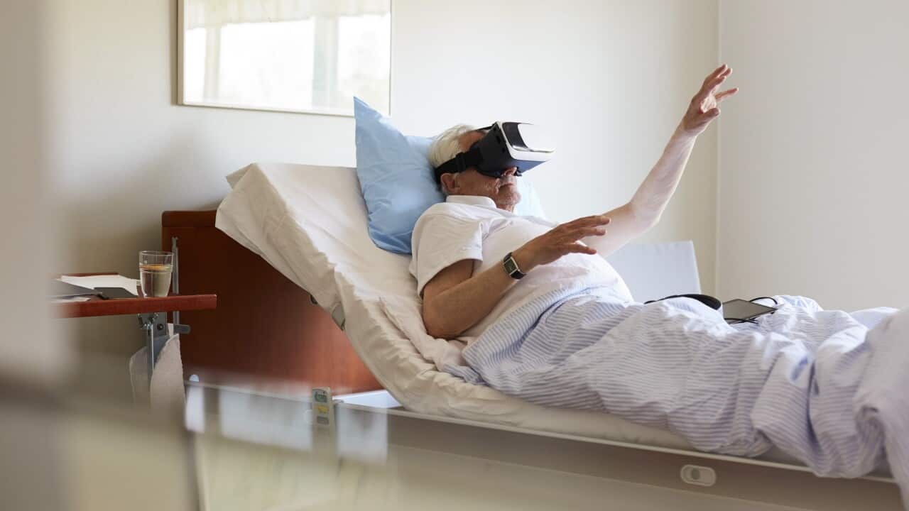 Senior man gesturing while using VR glasses on bed in hospital ward