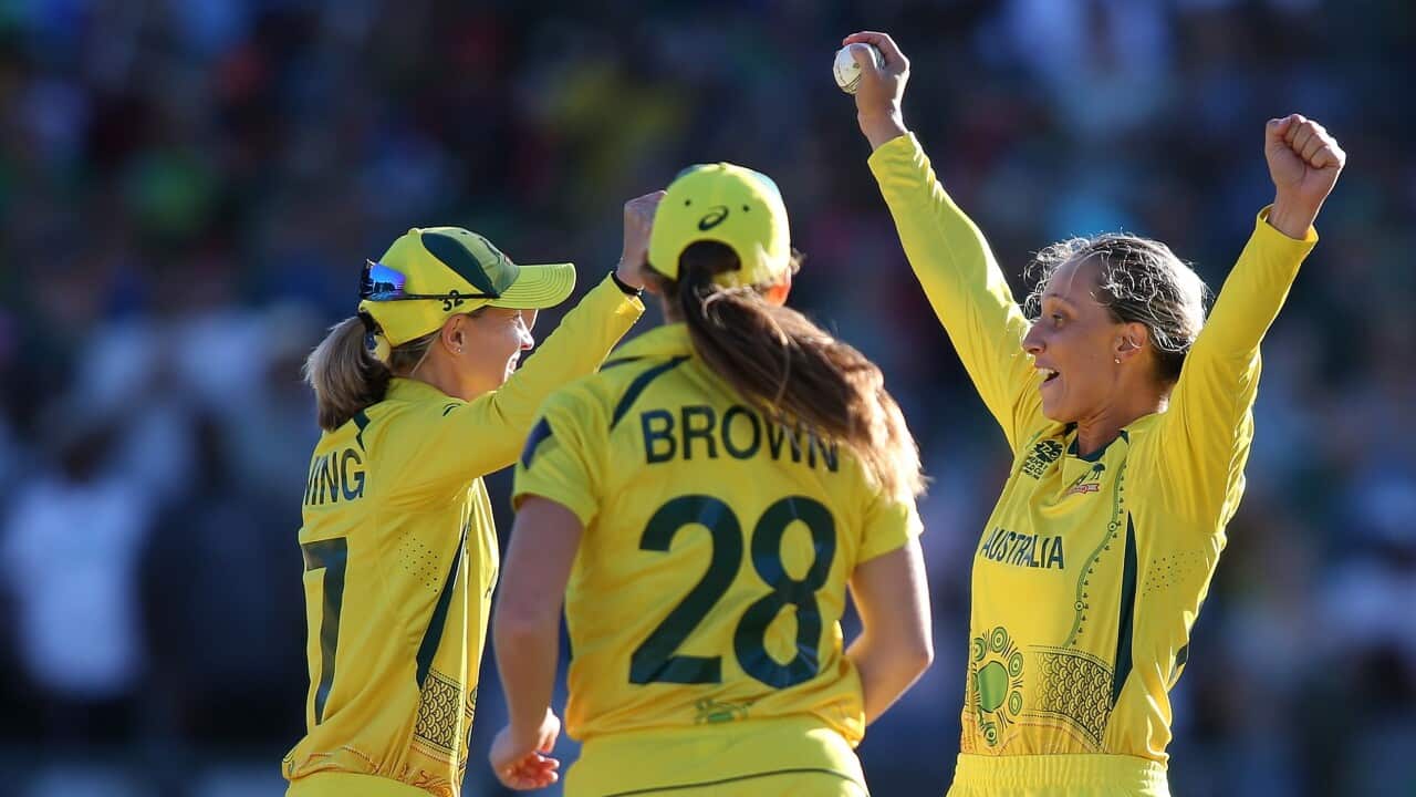 Three Australian women in cricket uniforms cheering