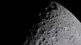 A photopgraph of the moon, taken at close range. Shadow obscures part of its face, highlighting crater edges.