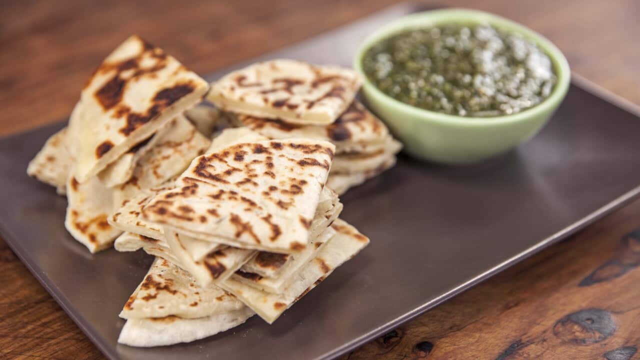 A pile of flatbread pieces sit on a rectangular tray. A Bowl of dip, out of focus sits behind the stack of bread.