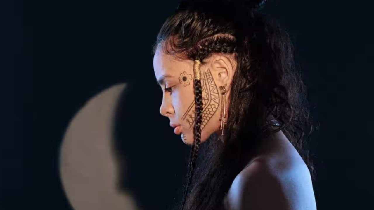 Side profile of woman's face with face tattoos and hair in plaits.
