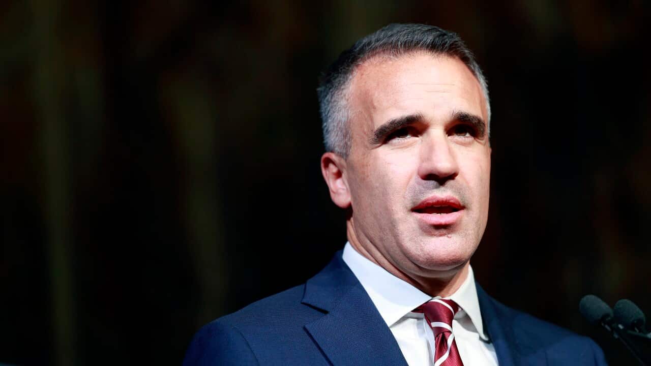 A close-up of a middle-aged man wearing a navy suit standing behind a microphone.