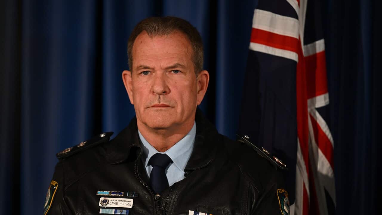 A man in a police uniform jacket standing in front of an Australian flag.