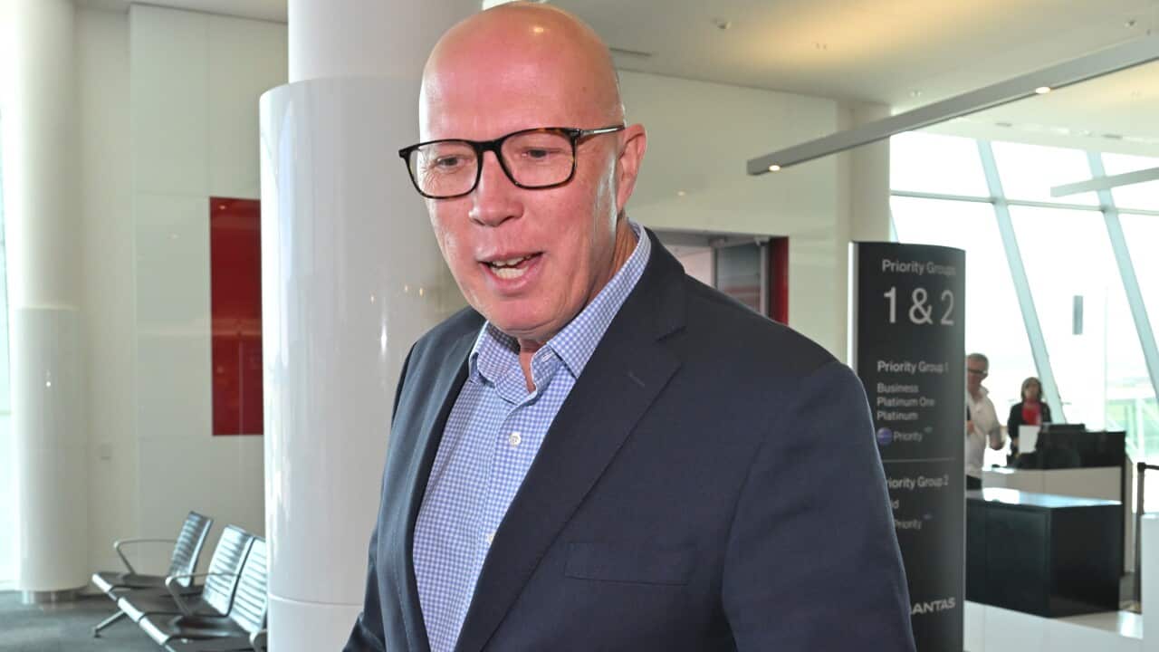 Former Opposition leader Peter Dutton, wearing a suit, tie and glasses, talking to journalists while walking inside and airport.