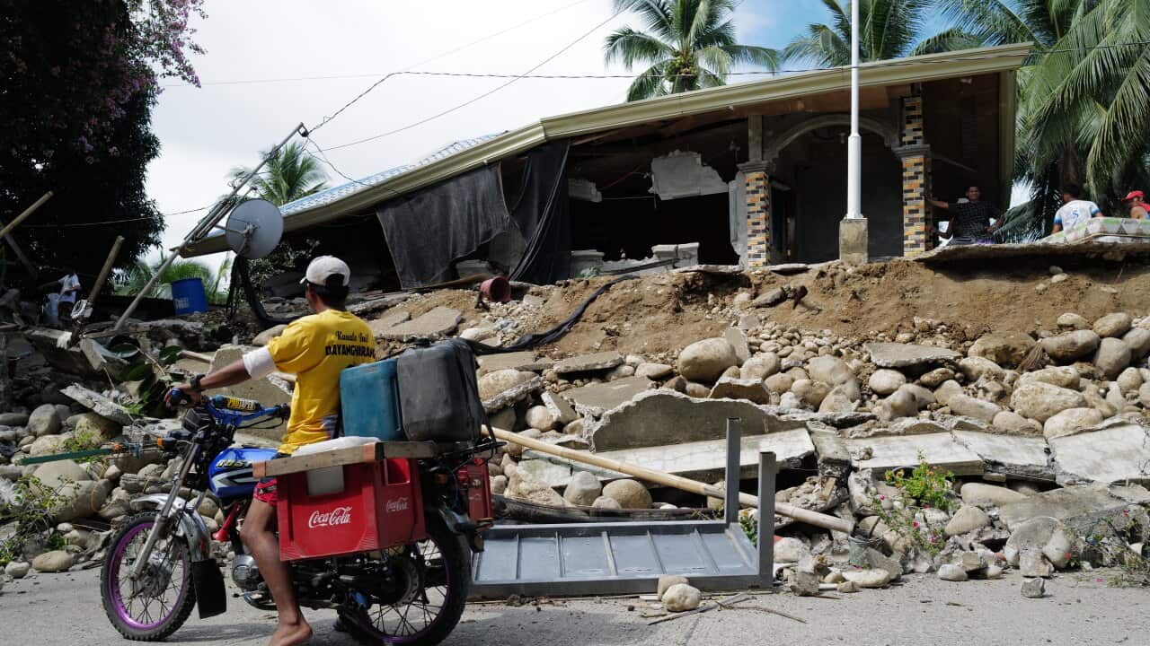 A man on a motorcycle in front of a heavily damaged home.