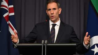Treasurer Jim Chalmers talks to media from a podium flanked with Australian flags