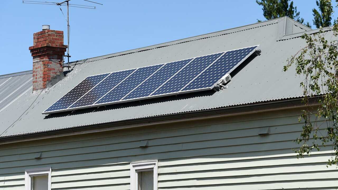 The view of a side of a house with solar panels on a corrugated tin roof.