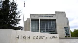 A concrete building has large glass windows. In front, a concrete pillar has the text 'High Court of Australia'.